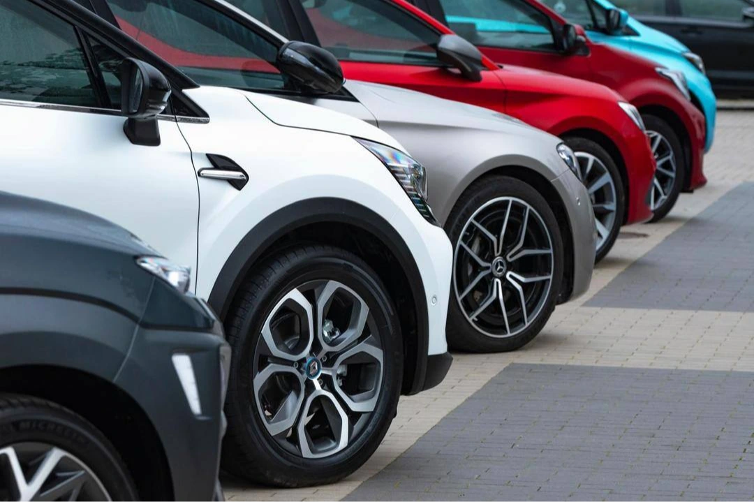 Reihe geparkter Autos auf Parkplatz, Detail von Felgen und Frontpartien